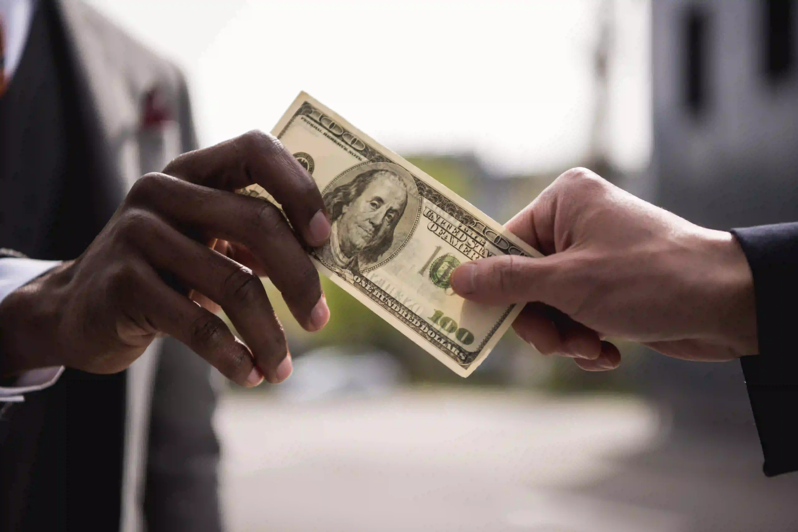 A man give 100 dollar note to the other man How Much Does Tattoo Removal Cost