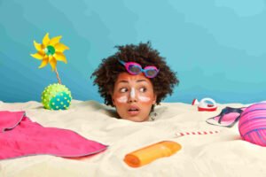 Young woman head with sunscreen cream face surrounded by beach accessories.